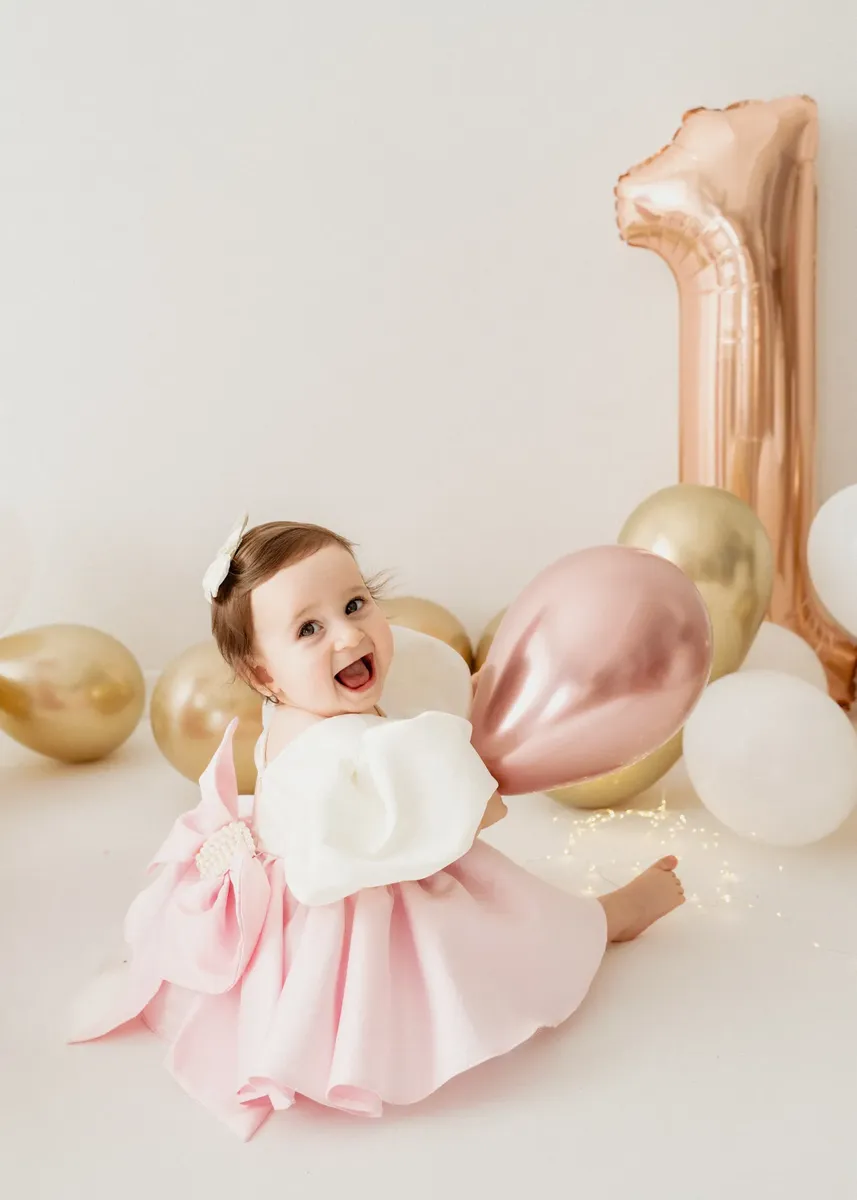 Bimba sorridente in abito rosa con palloncini dorati per il primo compleanno