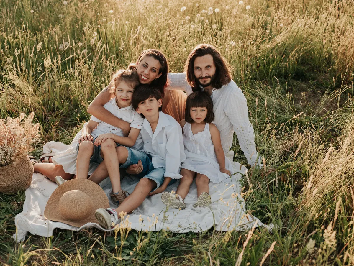Famiglia con tre bambini seduta su coperta in campo di grano dorato