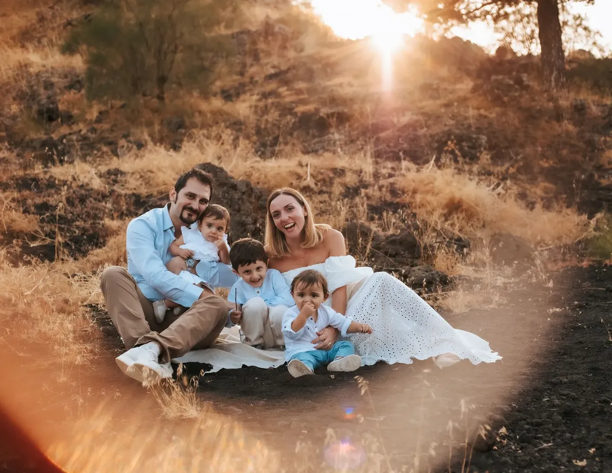 Famiglia con tre bambini piccoli seduta all'aperto al tramonto dorato