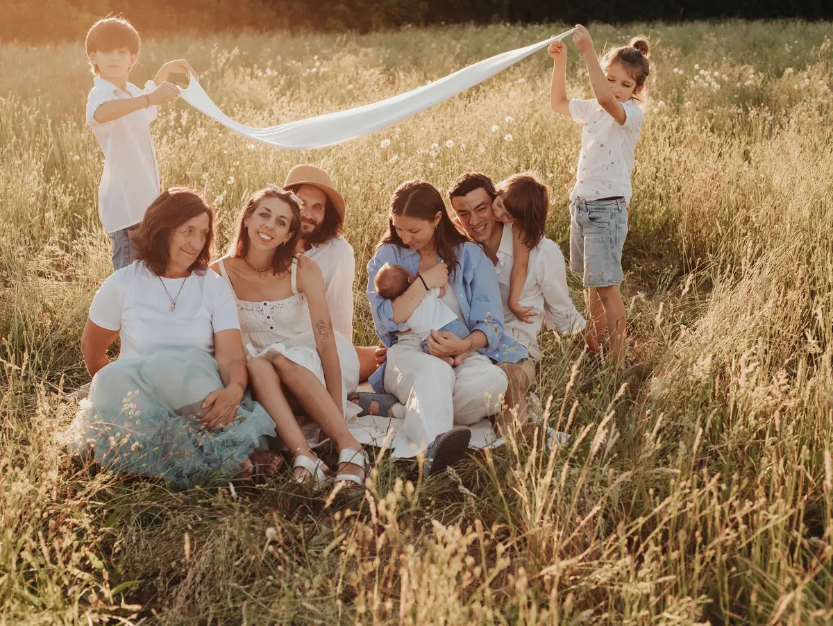 Famiglia allargata con neonato e bambini in un prato estivo, fotografia famiglia