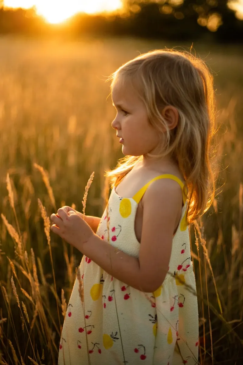Bambina bionda di profilo in campo di grano dorato al tramonto