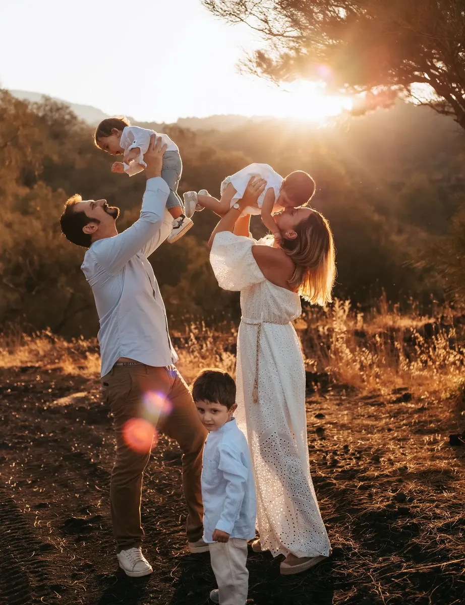 Genitori che sollevano in aria i due figli piccoli al tramonto, famiglia felice