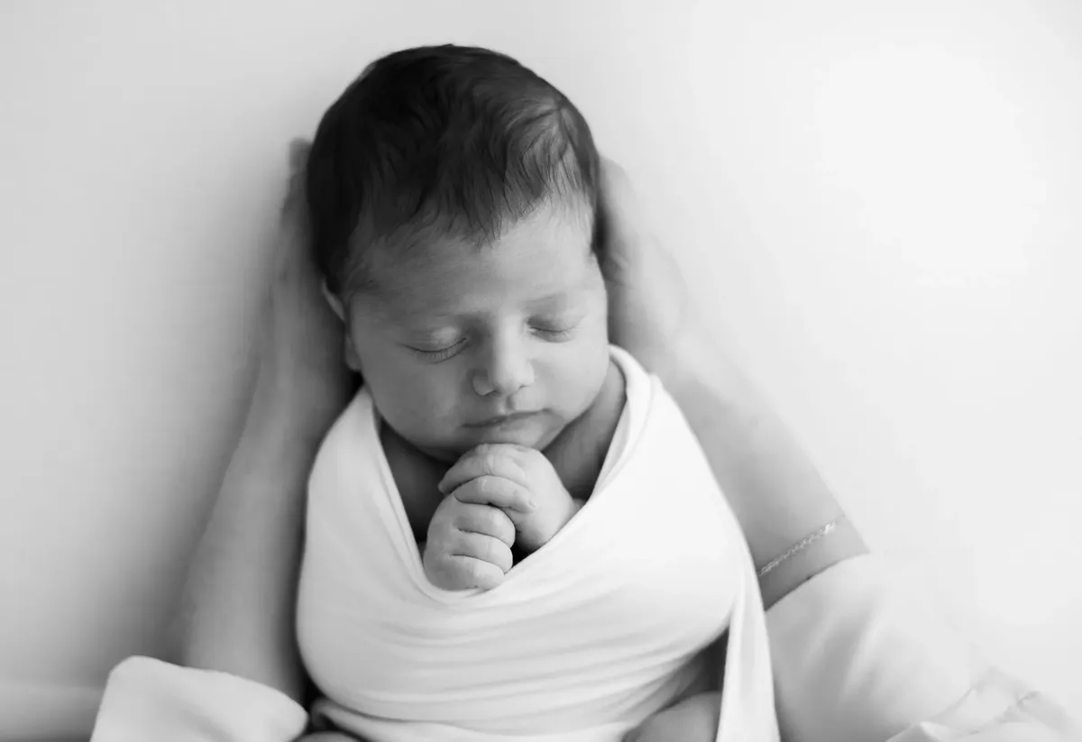 Neonato avvolto in fascia bianca tra le mani della mamma, ritratto intimo in bianco e nero