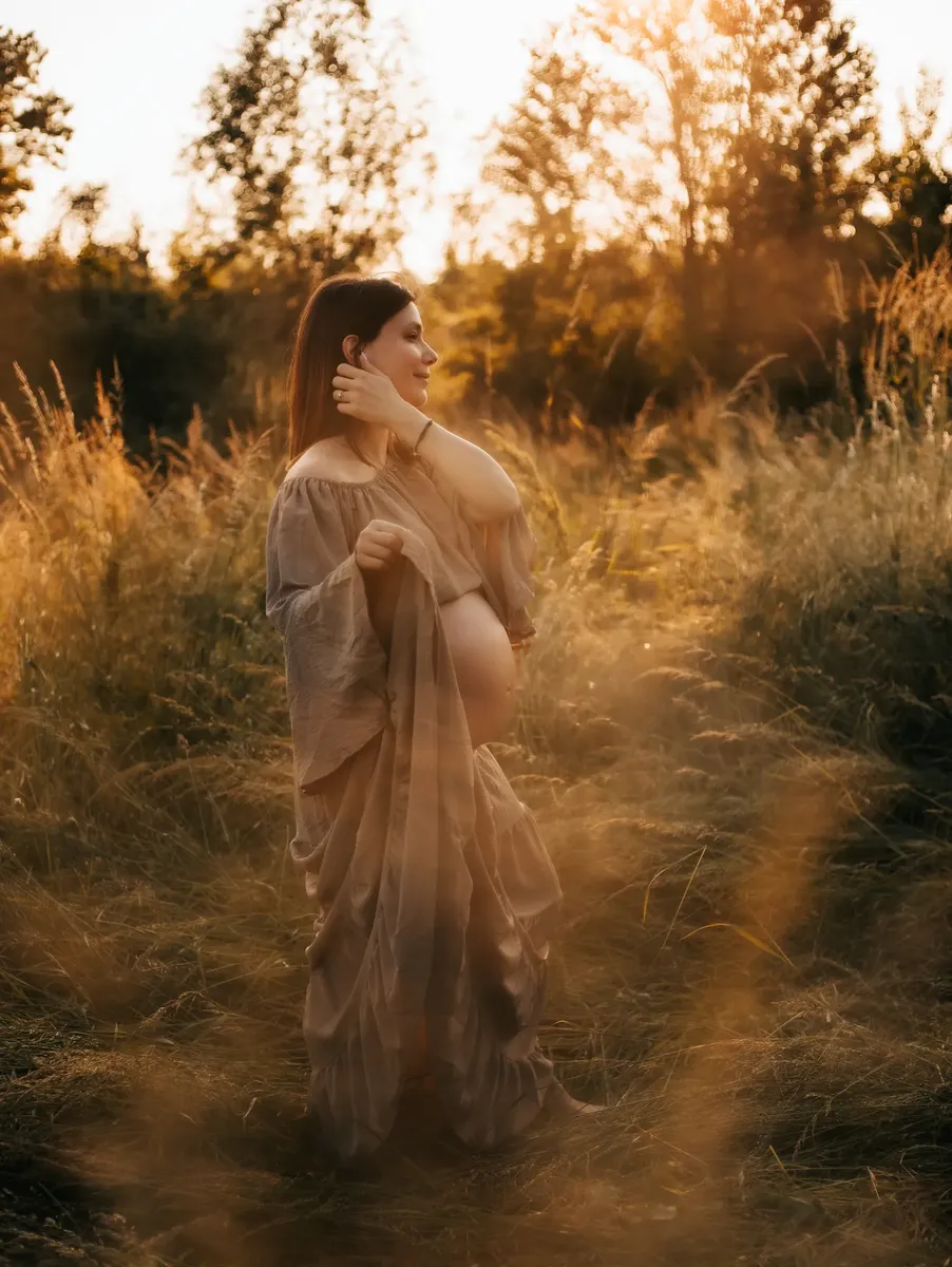 Donna incinta in abito beige aperto cammina in un sentiero dorato al tramonto