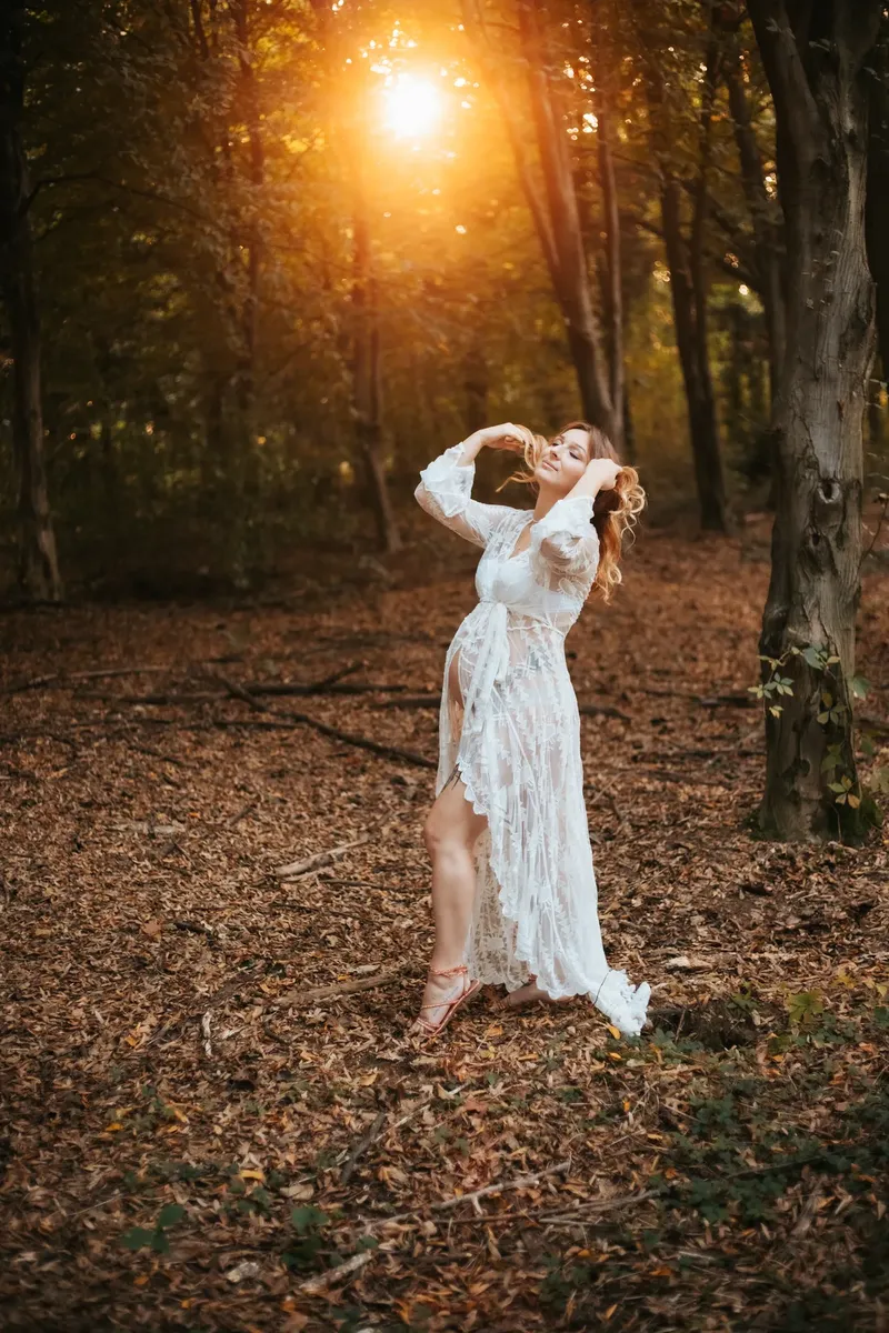 Donna incinta in abito bianco di pizzo danza nel bosco con luce autunnale