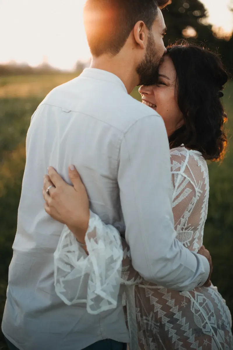 Coppia in attesa abbracciata teneramente con bacio nel prato al tramonto