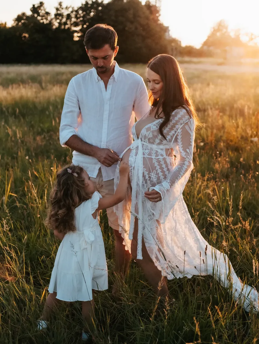 Famiglia in attesa con figlia nel prato al tramonto con abito di pizzo bianco