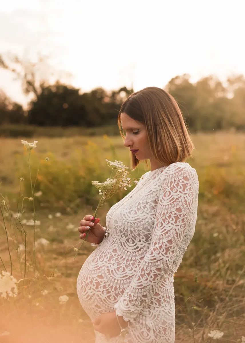 Donna incinta in abito di pizzo bianco con fiori di campo al tramonto