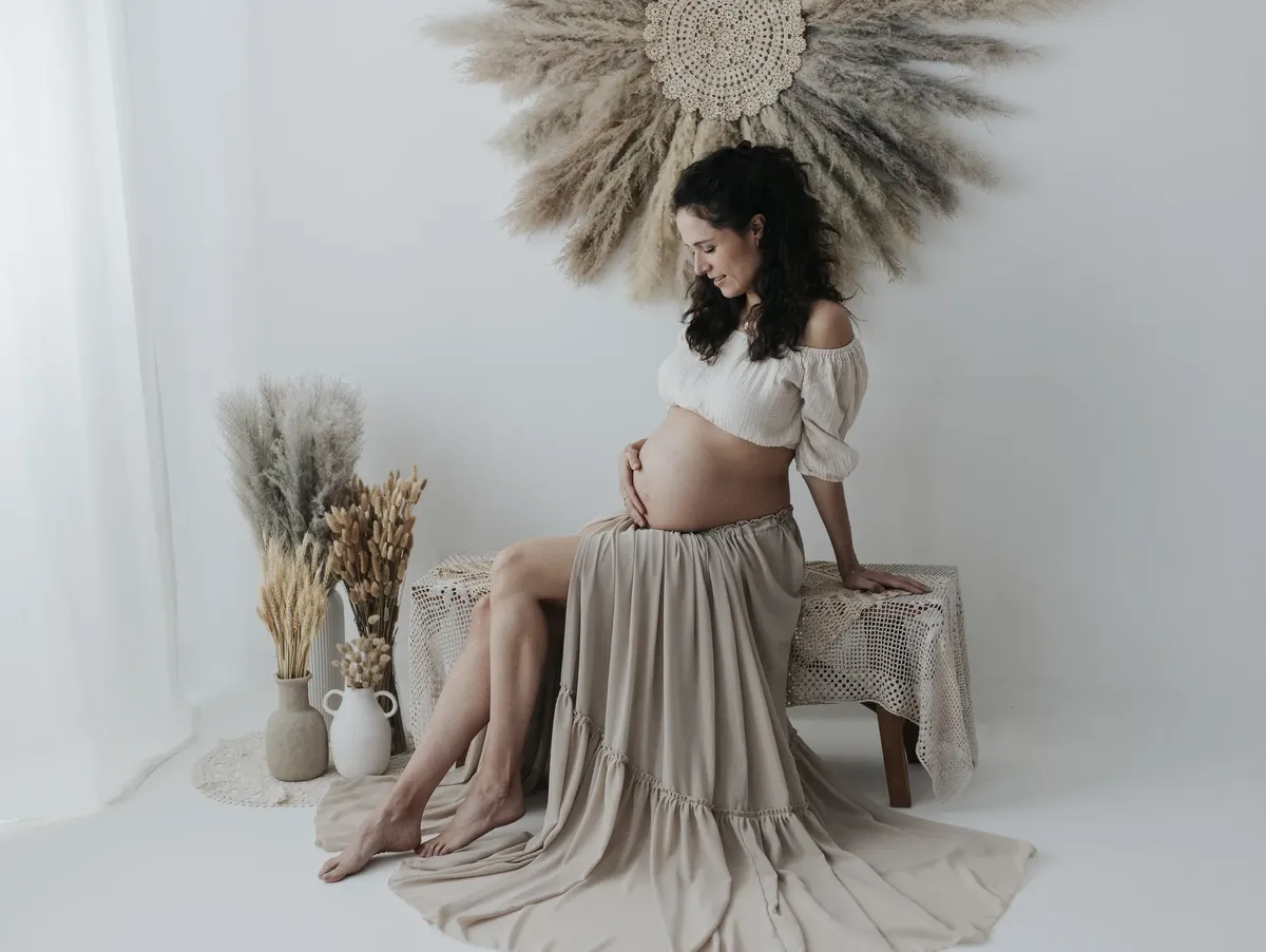 Futura mamma seduta con gonna lunga beige e decorazioni boho in studio Milano