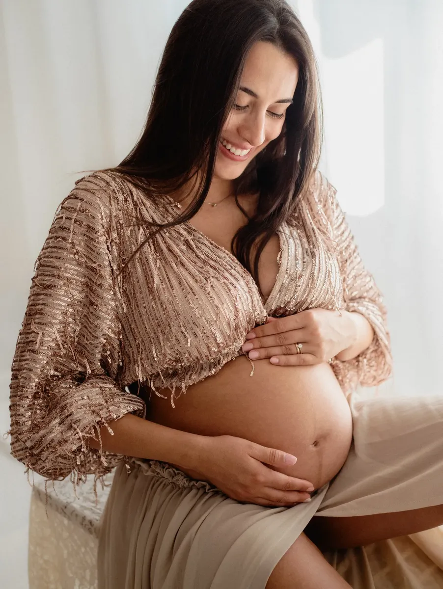 Primo piano sorridente di donna incinta con top brillante dorato, fotografo maternita Milano