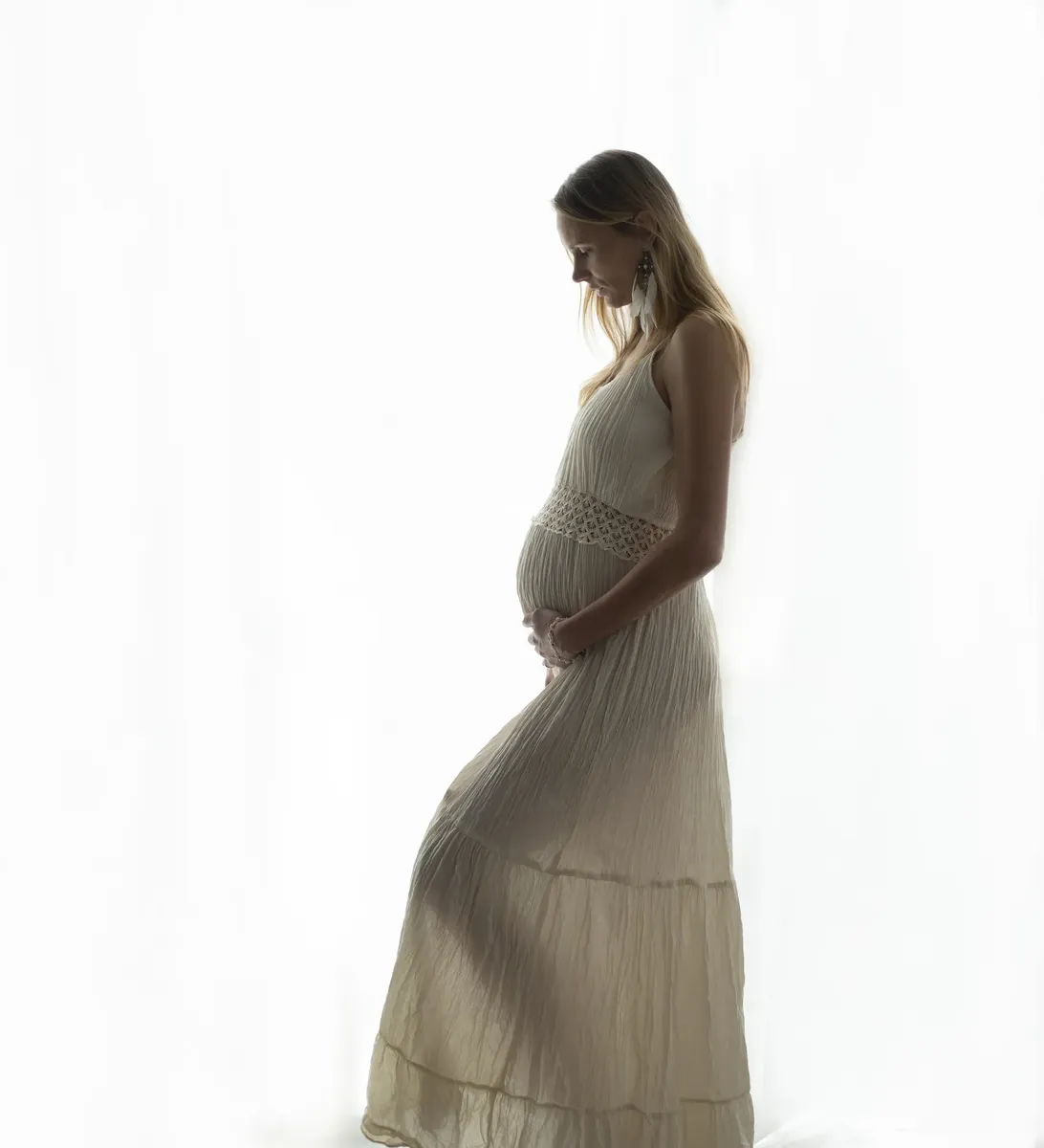 Silhouette profilo di futura mamma in abito lungo beige con luce naturale in studio