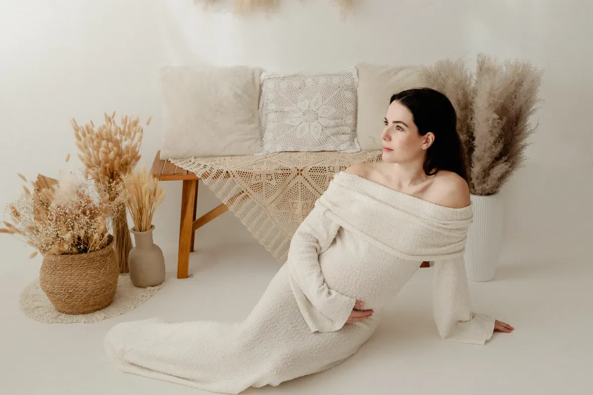 Futura mamma seduta a terra con abito a maglia bianco e set boho con pampa