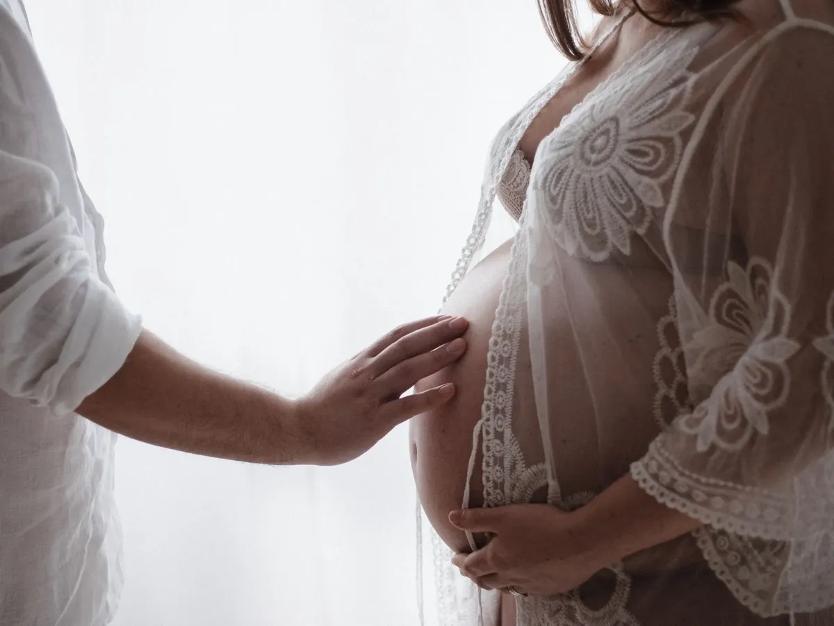 Dettaglio mano del partner sul pancione con vestaglia pizzo bianco, servizio premaman