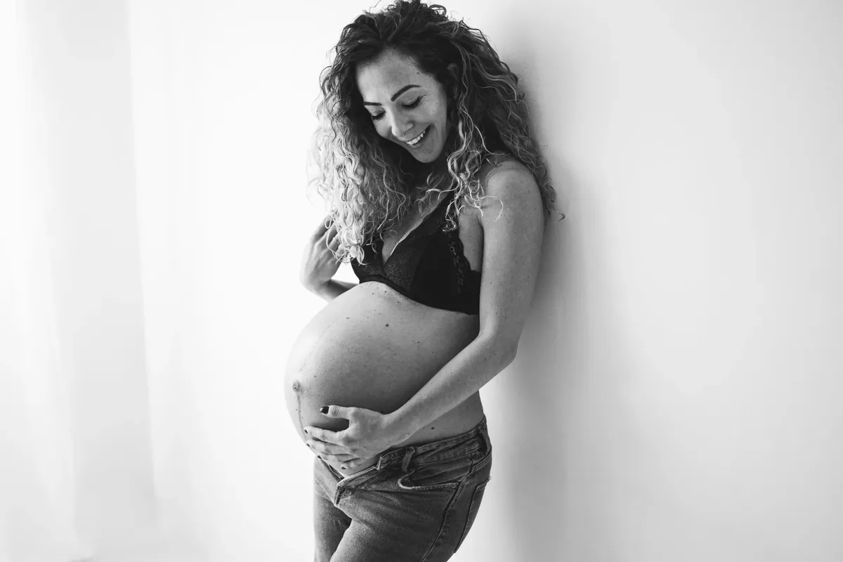 Donna incinta sorridente in bianco e nero con jeans e top nero, pancione scoperto