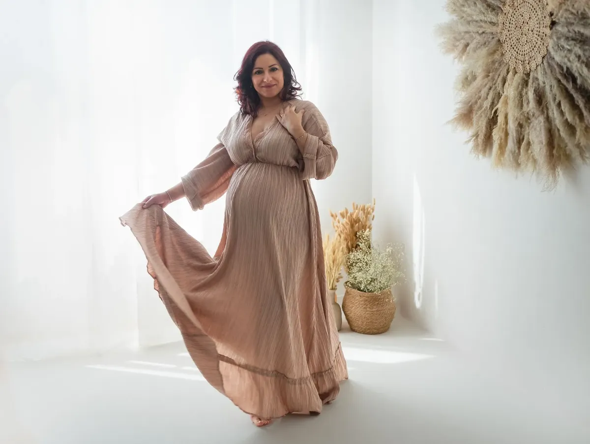 Donna incinta in abito lungo rosa cipria con decorazioni boho in studio Milano
