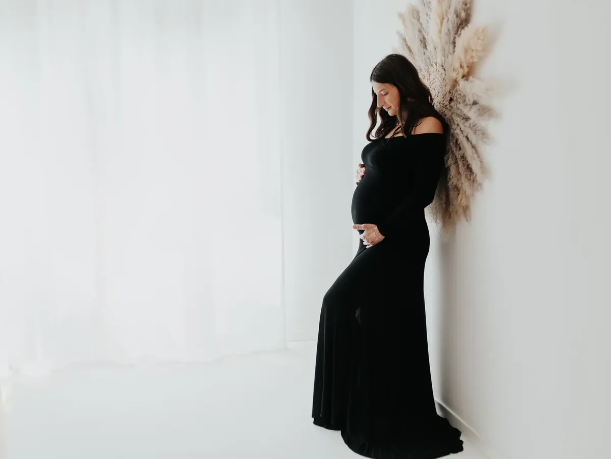 Servizio fotografico maternita Milano, donna in abito nero lungo appoggiata alla parete con pampa