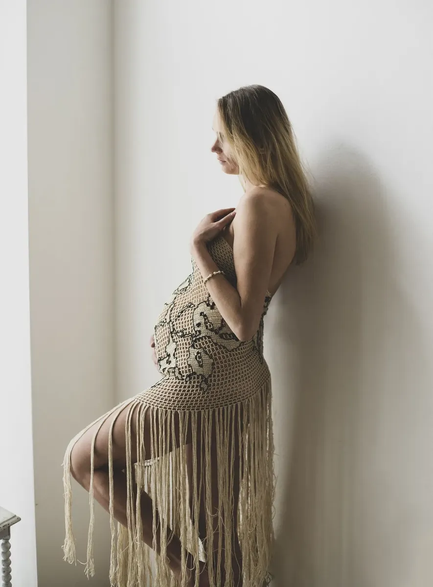 Gestante appoggiata al muro in abito crochet con frange beige, servizio premaman Milano