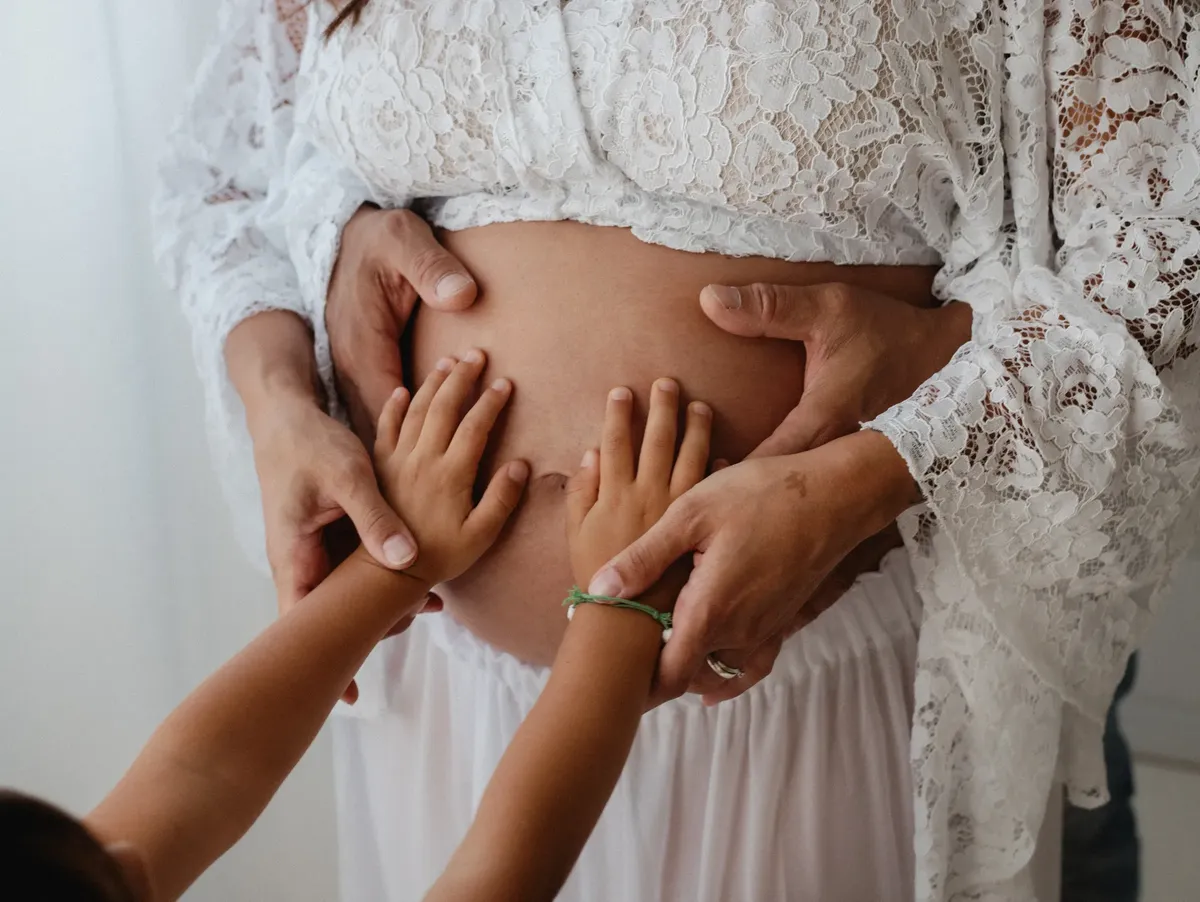 Mani di bambino e mamma sul pancione con abito di pizzo bianco in studio