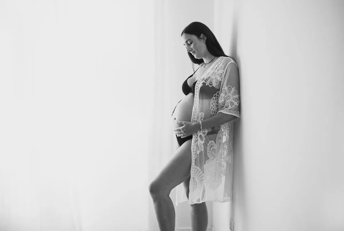 Donna incinta in kimono di pizzo bianco appoggiata al muro in bianco e nero