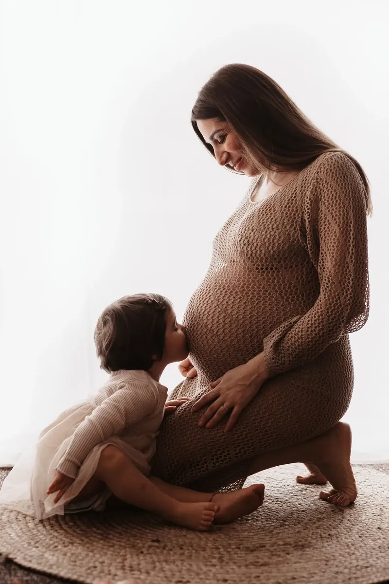 Bimba bacia il pancione della mamma in abito a rete beige, servizio premaman tenero