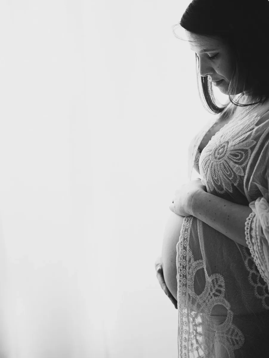 Ritratto intimo in bianco e nero di gestante in pizzo che accarezza il pancione