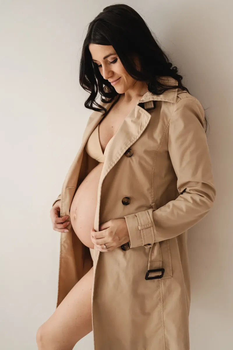 Donna incinta in trench beige aperto sul pancione, servizio fotografico premaman Milano