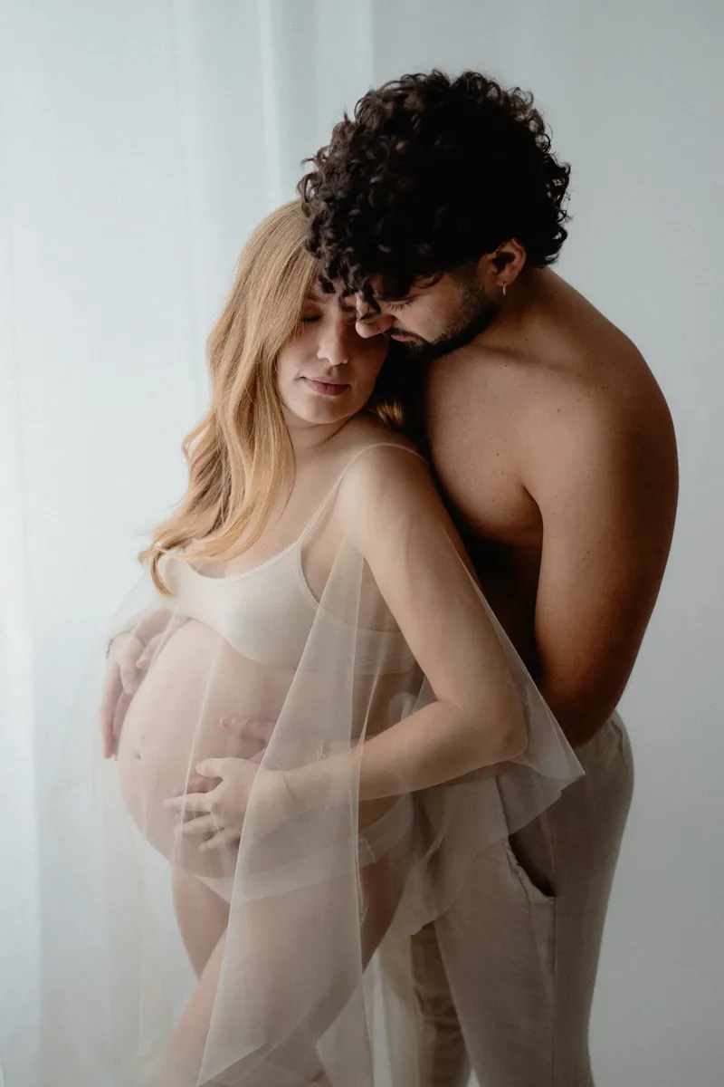 Coppia in attesa abbracciata con velo trasparente e luce morbida in studio