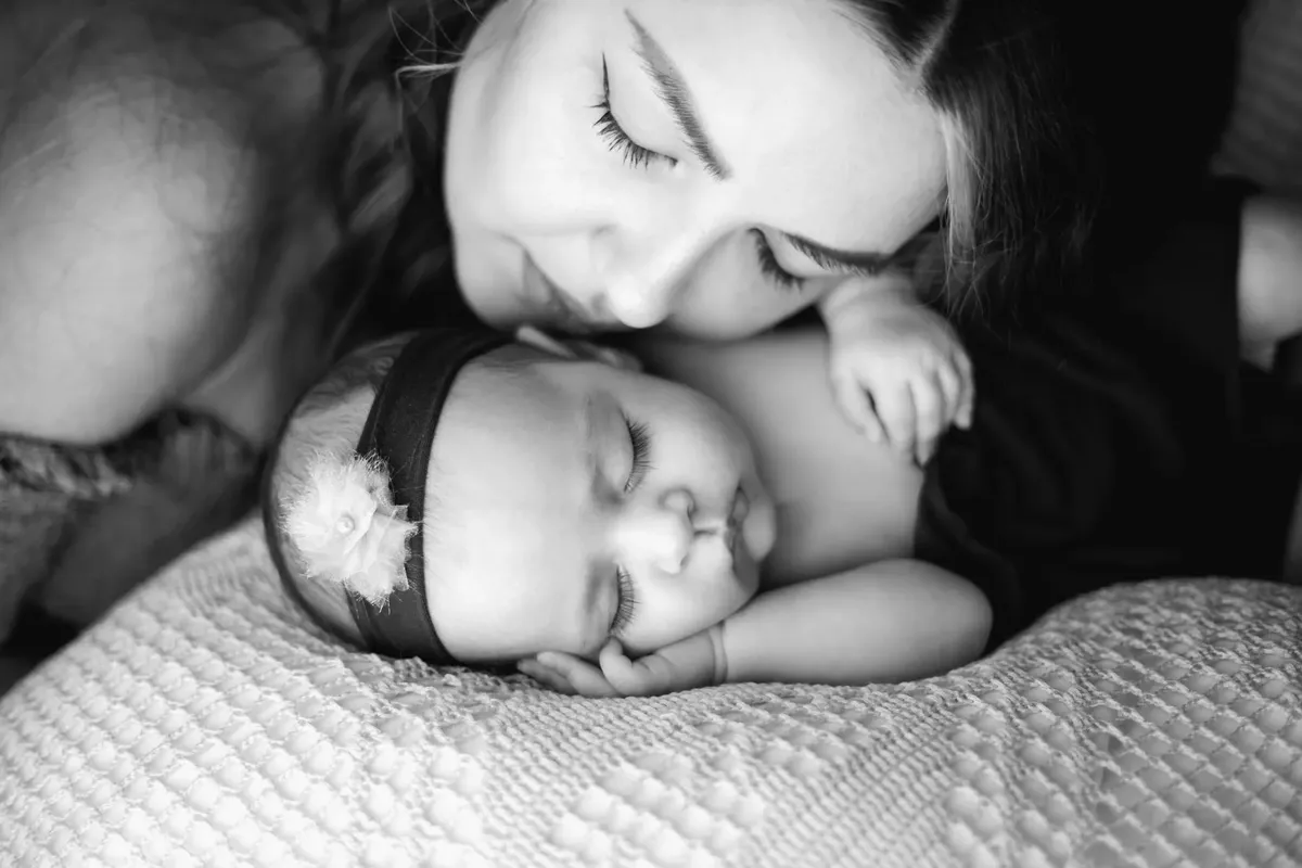 Mamma che bacia la sua neonata addormentata, foto newborn in bianco e nero