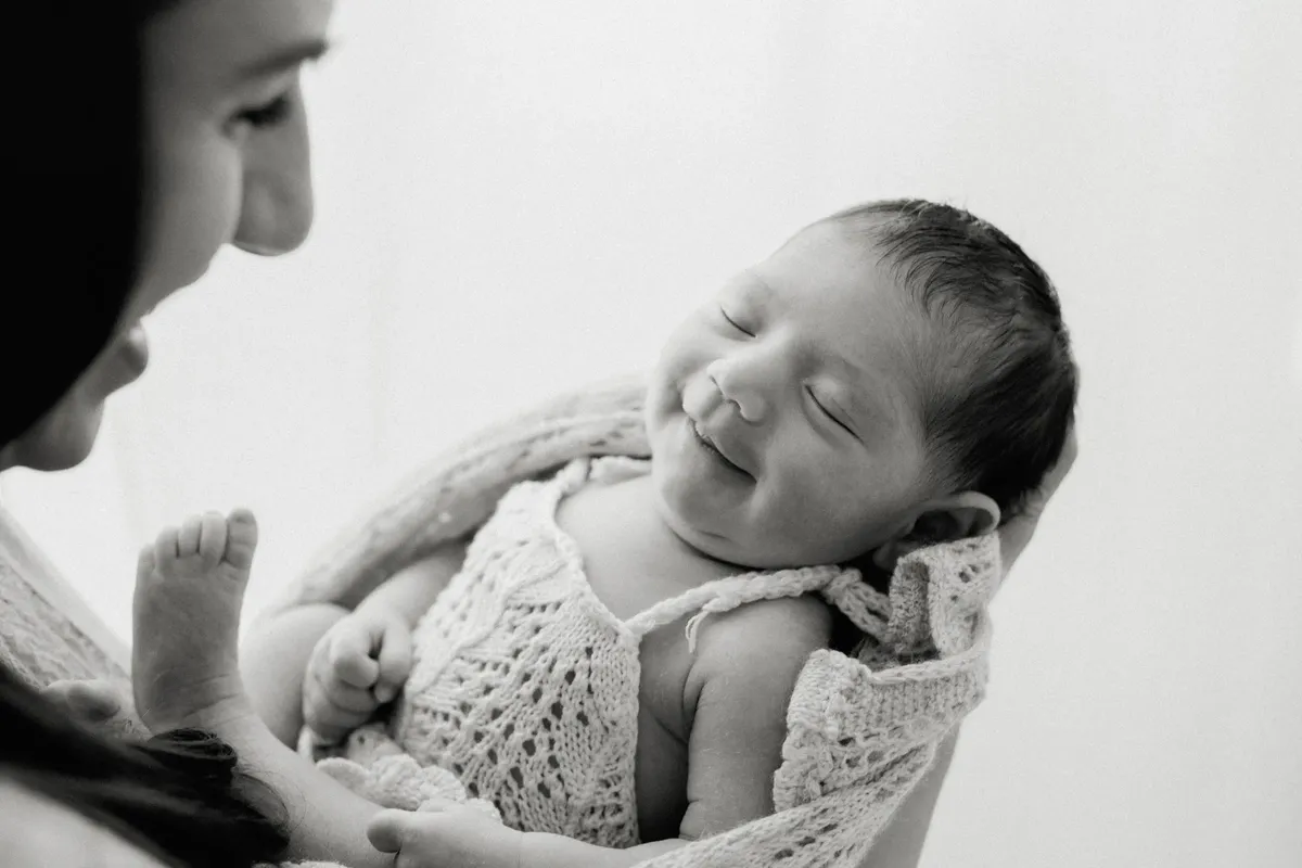Neonato sorridente in braccio alla mamma avvolto in copertina a maglia