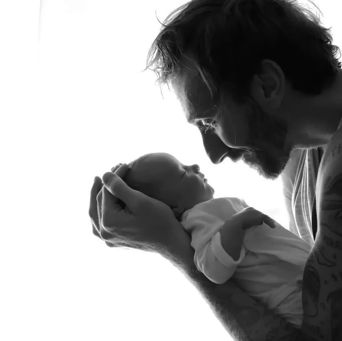 Papà che tiene il neonato tra le mani in controluce, servizio newborn Milano