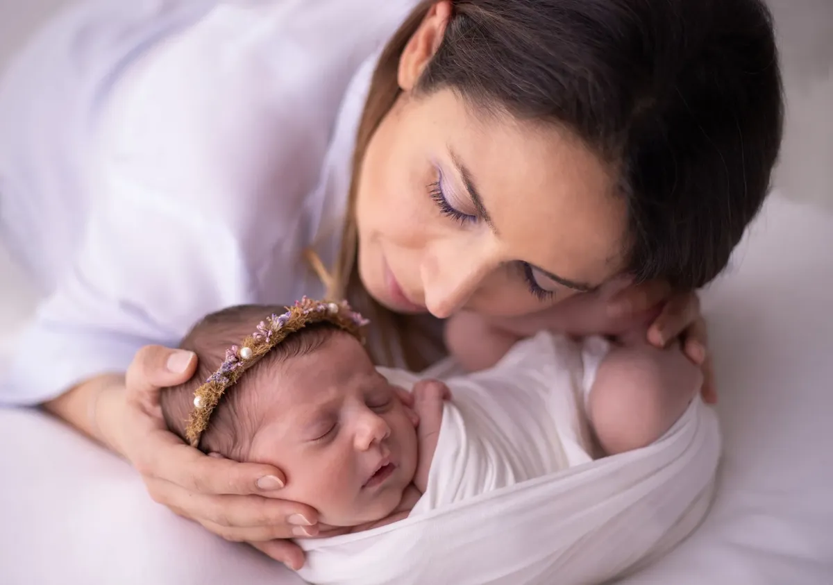 Mamma con neonata avvolta in wrap bianco e coroncina floreale, foto newborn Milano