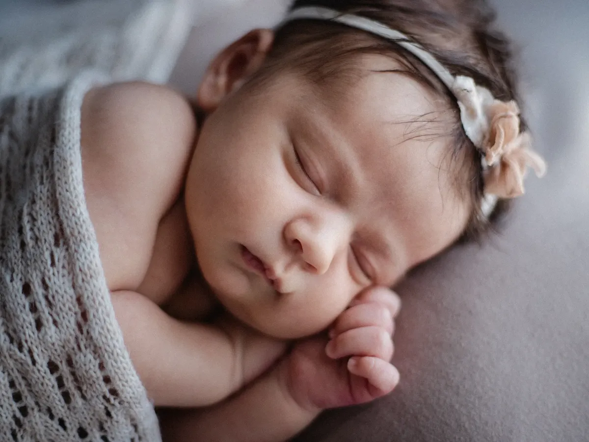 Primo piano di neonata che dorme con fascetta e copertina a maglia grigia