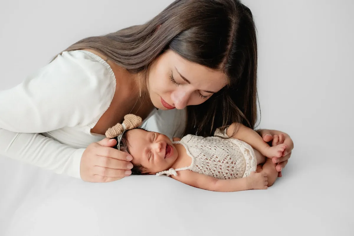Mamma che guarda la neonata sorridente con vestitino e fiocco all'uncinetto