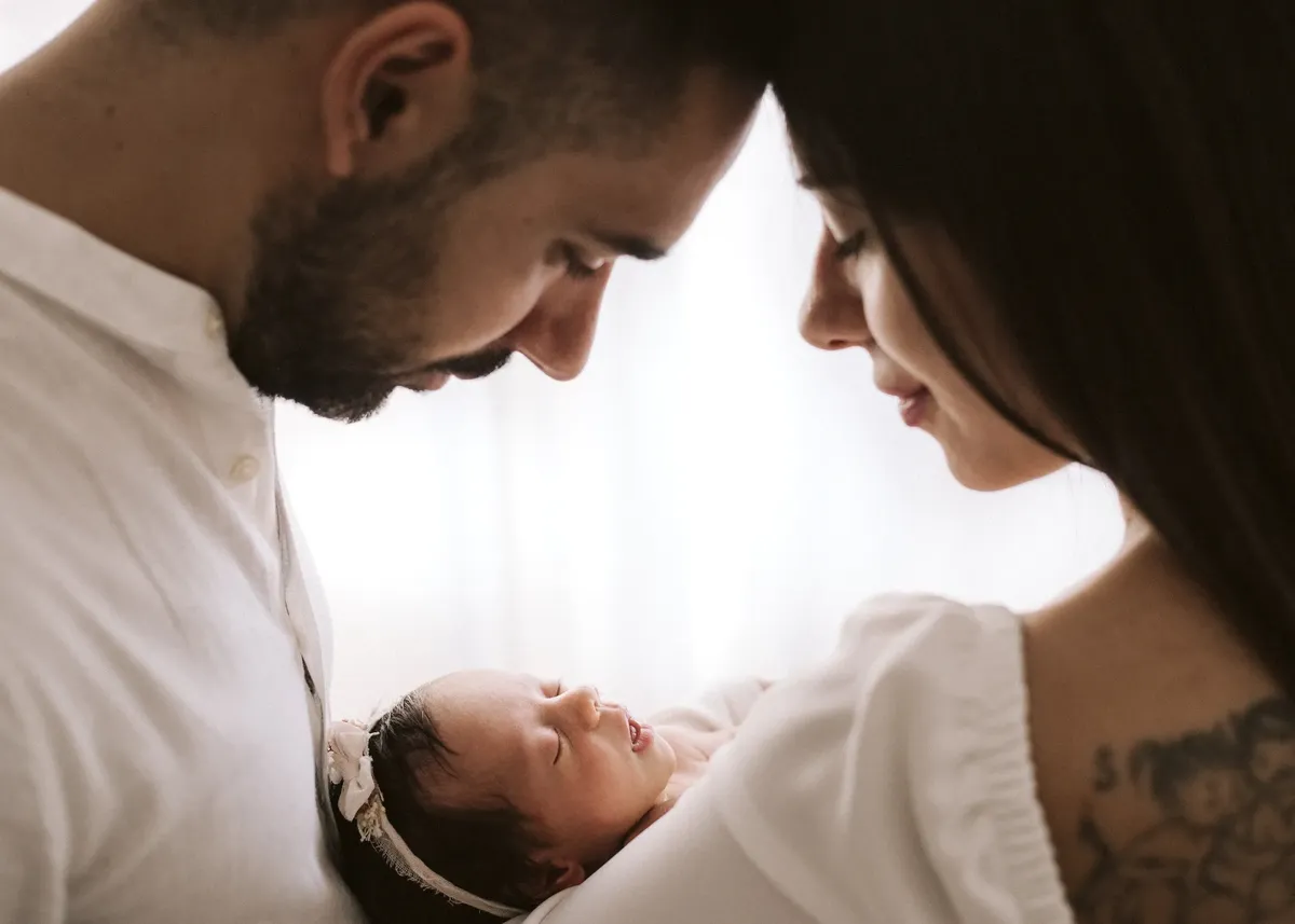 Genitori con neonata tra le braccia in controluce, servizio fotografico newborn Milano