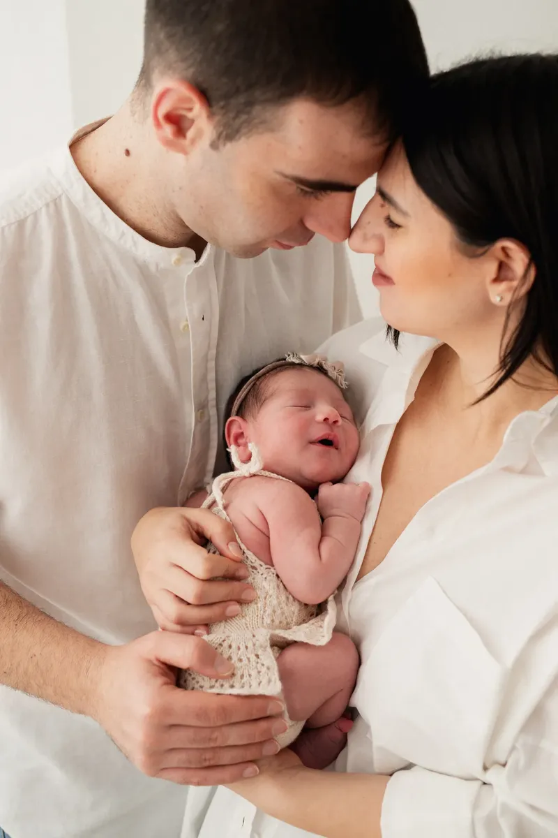 Genitori in bianco che tengono la neonata sorridente con vestitino a maglia