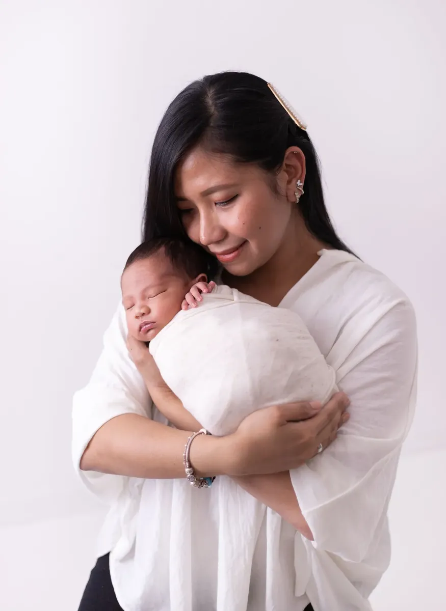 Mamma sorridente che tiene in braccio il neonato avvolto in wrap bianco