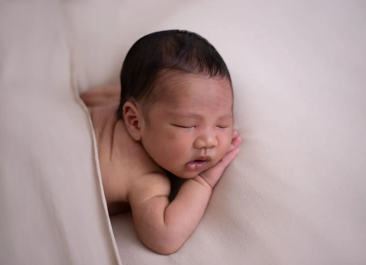 Neonato che dorme con manina sulla guancia su coperta color crema