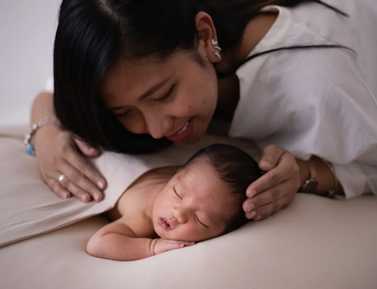 Mamma sorridente accarezza il neonato addormentato su sfondo beige, foto newborn