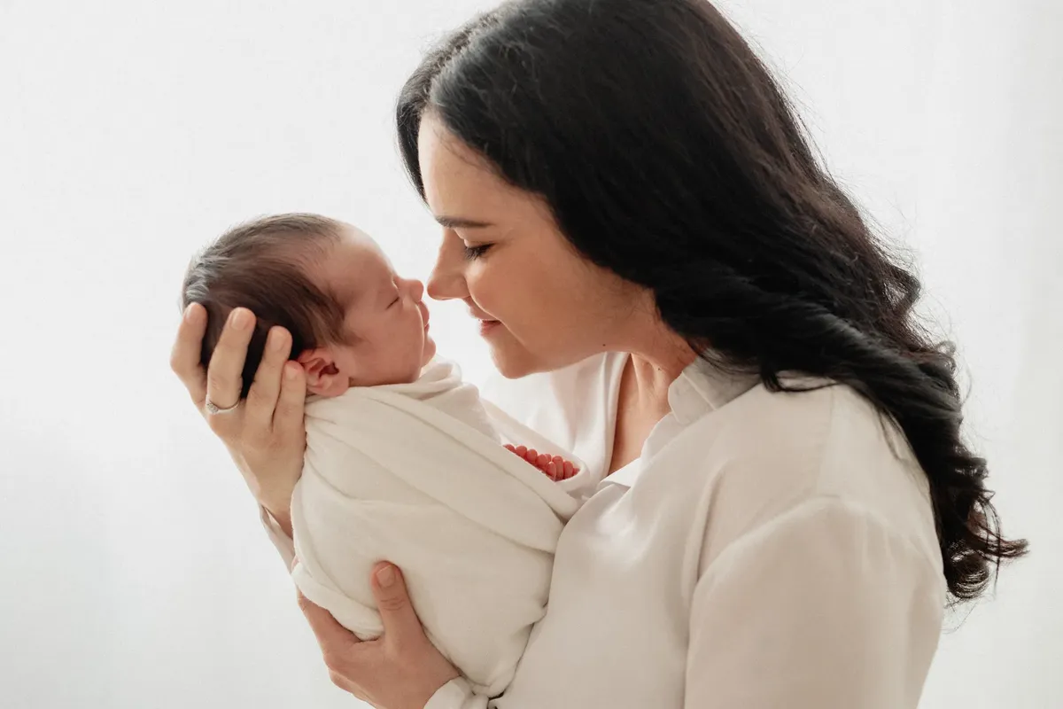 Mamma che tocca il nasino del neonato avvolto in wrap, profilo su sfondo bianco