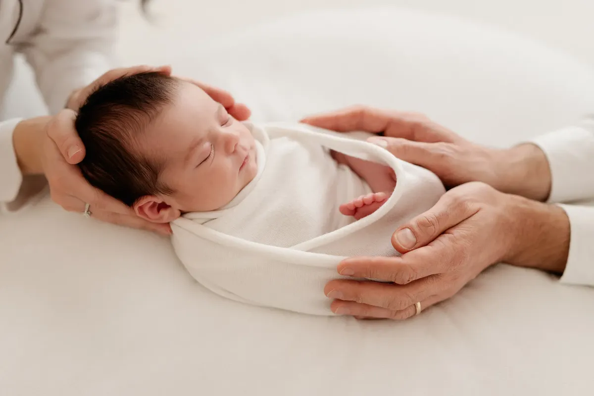 Mani dei genitori che sostengono il neonato avvolto in wrap bianco