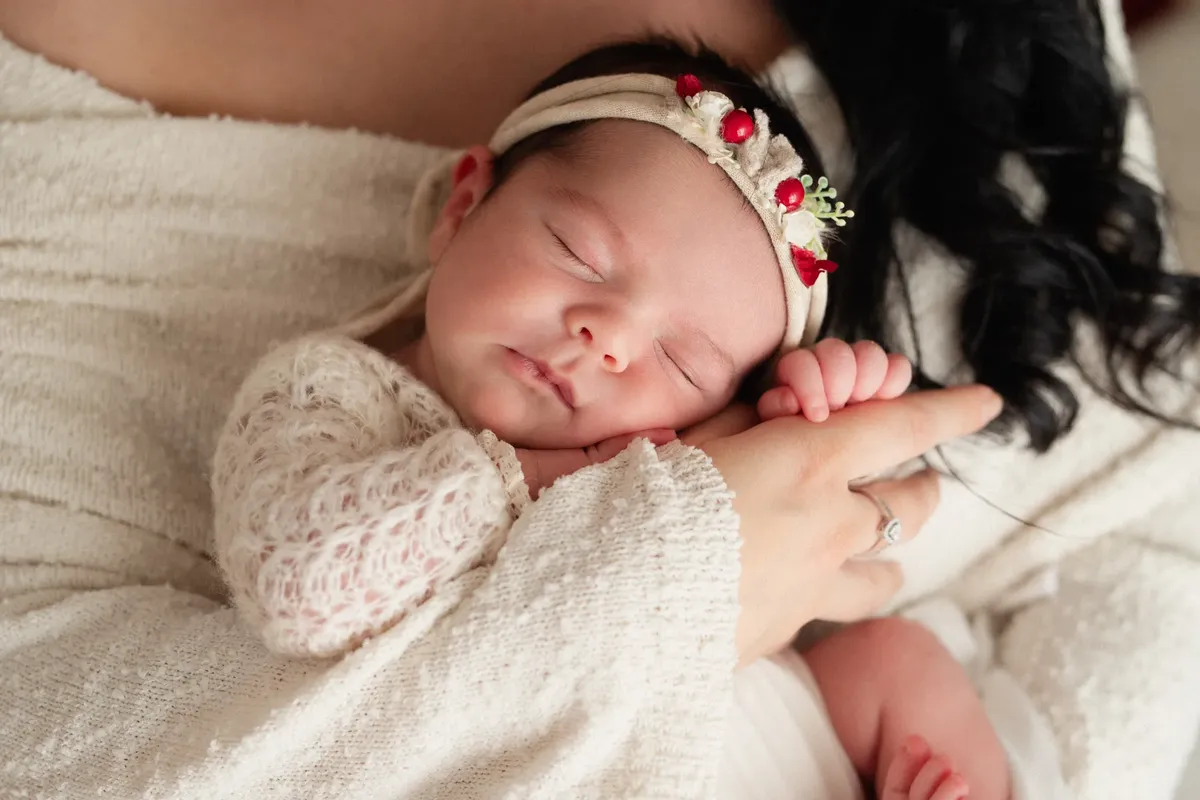 Neonata che dorme sulla mano della mamma con fascetta floreale rossa e vestitino