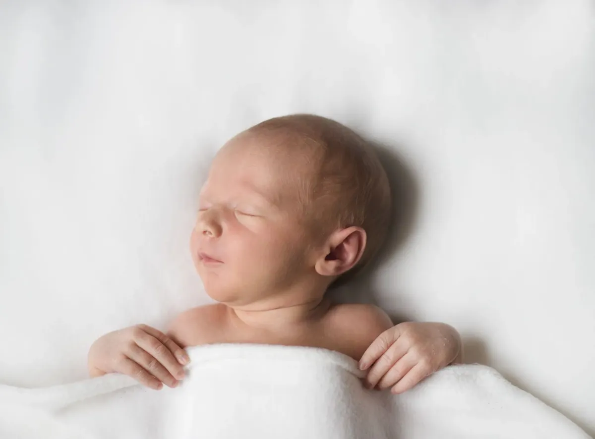 Neonato che dorme su coperta bianca con braccia fuori, ritratto minimalista
