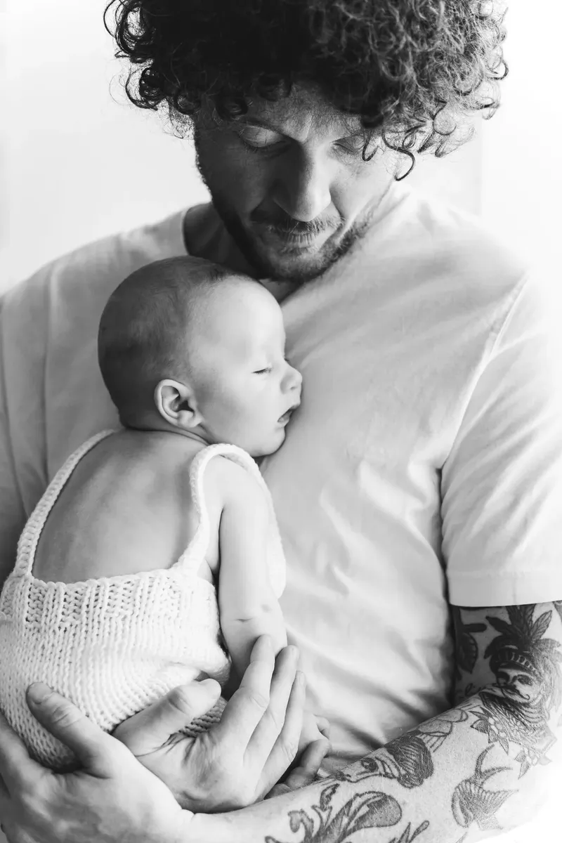 Papà che tiene il neonato in braccio con vestitino a maglia, bianco e nero