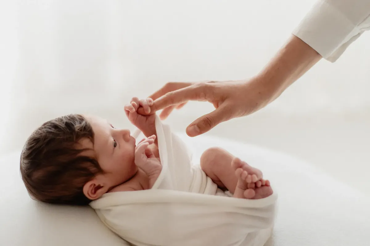 Neonato sveglio avvolto in wrap bianco che stringe il dito del papà