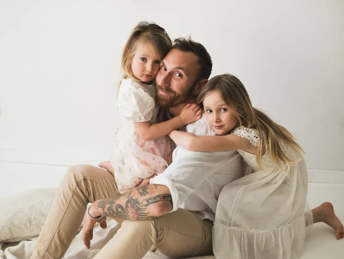 Papà seduto in studio con le due figlie in braccio, ritratto di famiglia spontaneo e tenero
