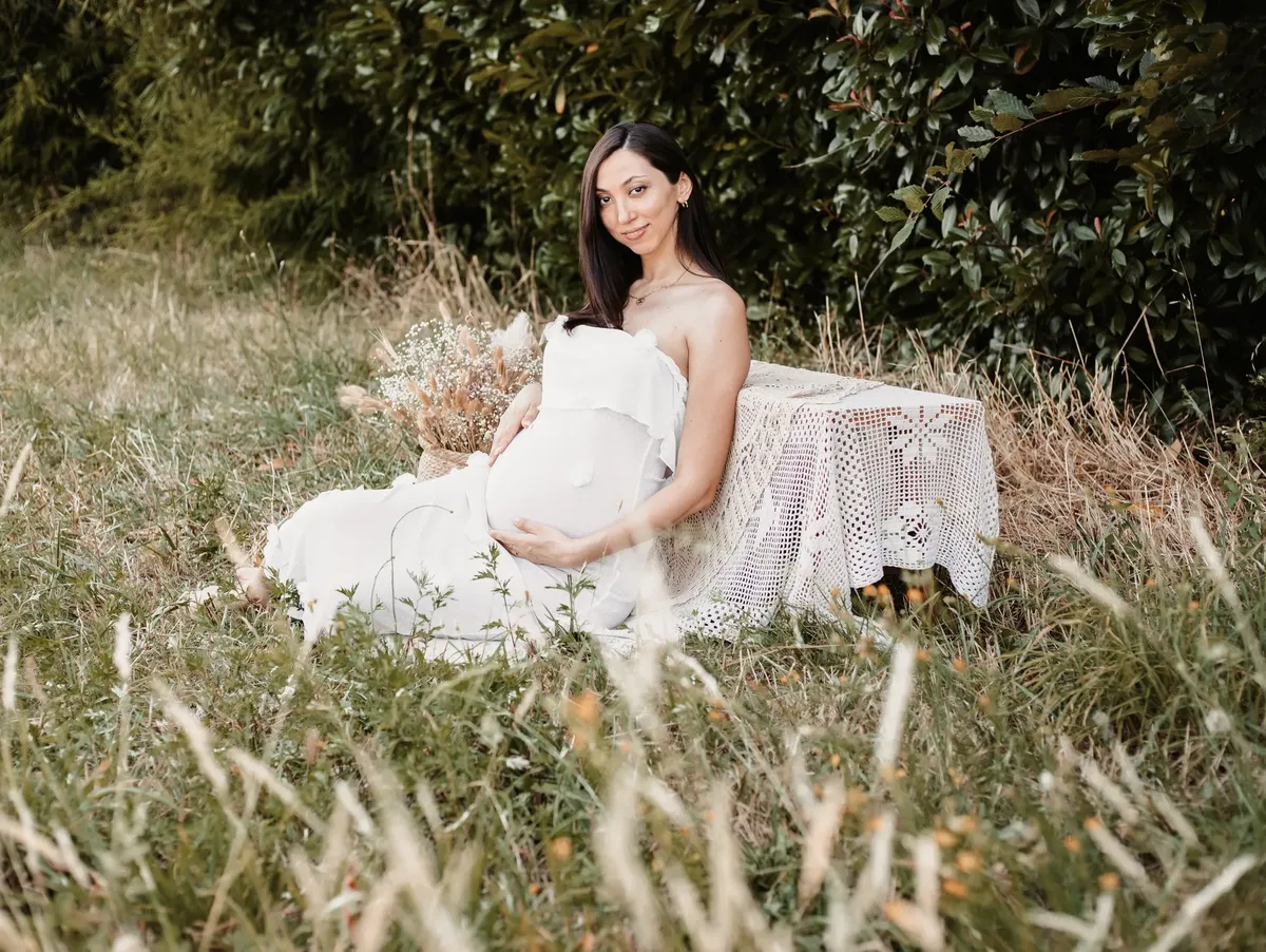 Futura mamma seduta nell erba con abito bianco e bouquet di fiori secchi, servizio maternità in esterna