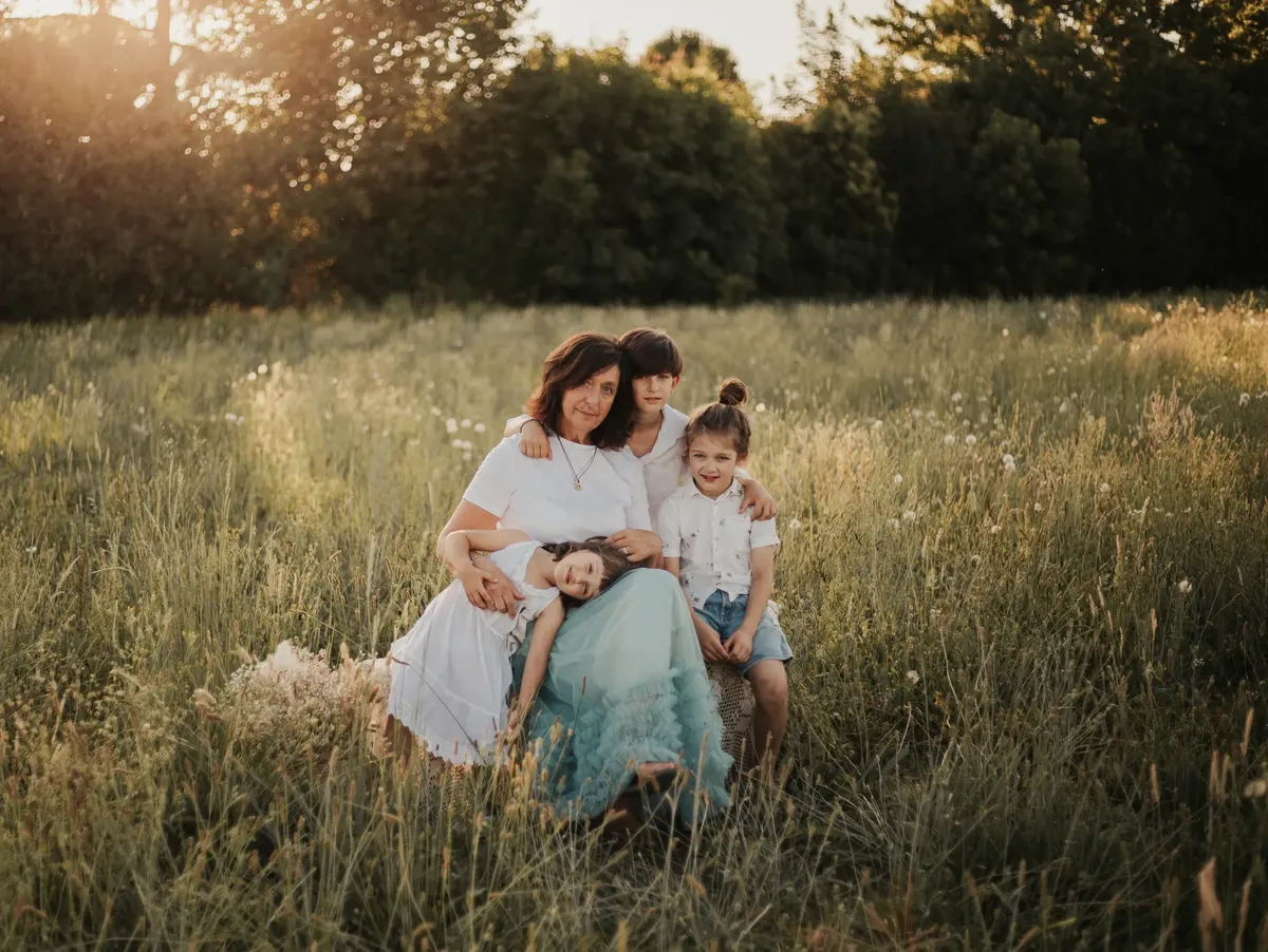 Mamma con tre bambini abbracciati in un prato al tramonto, ritratto di famiglia spontaneo